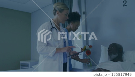 Doctor in white coat holding tablet and nurse arranging flowers beside patient in hospital room Doctor in white coat holding tablet and nurse arranging flowers beside patient in hospital room 135817949