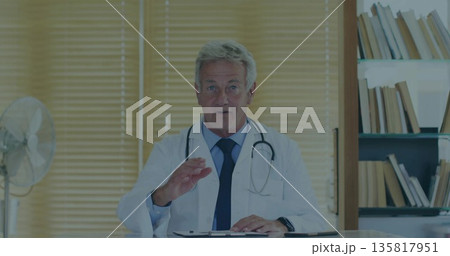 Gesturing doctor in lab coat and tie sitting at consultation desk, with clipboard stethoscope fan Gesturing doctor in lab coat and tie sitting at consultation desk, with clipboard stethoscope fan 135817951