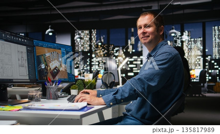 Portrait of male engineer uses architectural software and blueprints for 3D render of a home interior. Program allows to configure furniture and design elements for a virtual layout. Camera A. Portrait of male engineer uses architectural software and blueprints for 3D render of a home interior. Program allows to configure furniture and design elements for a virtual layout. Camera A. 135817989