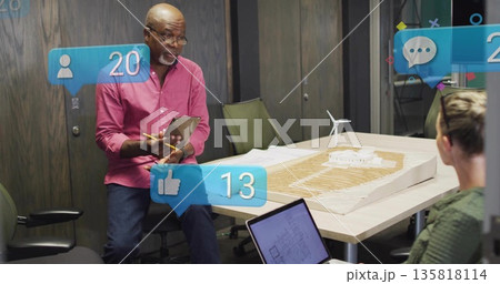 Presenting architect wearing pink shirt and jeans at conference table, with scale model, tablet Presenting architect wearing pink shirt and jeans at conference table, with scale model, tablet 135818114