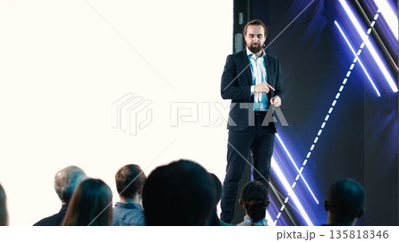 Male CEO presenting new mobile phone product launch on stage with premiere of modern smartphone interface. Entrepreneur introduces innovation and development with product release. 135818346