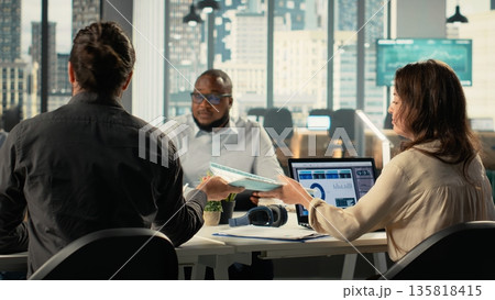 Business people greeting each other in office before a briefing meeting, colleagues discuss budgeting and project development. Diverse work team reviews reports and data on laptop. Business people greeting each other in office before a briefing meeting, colleagues discuss budgeting and project development. Diverse work team reviews reports and data on laptop. 135818415