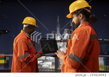 Drilling ship crew uses laptop to study geological maps for fossil fuel deposits. Offshore platform teamworking colleagues perform site assessment with digital mapping tech on notebook 135818563