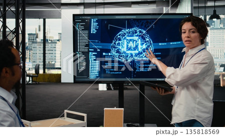 Investors gathered in tech startup boardroom to do deep dive into artificial intelligence. Programmer showcasing latest innovations in AI sector at corporate event in front of businesspeople, camera A 135818569