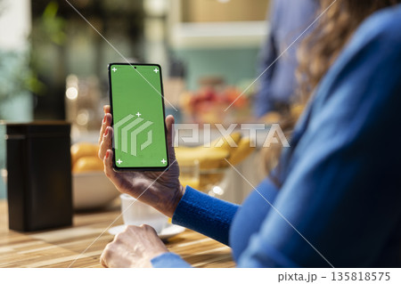 Green screen on mobile phone where aged person enjoys calm morning routine, serving coffee and pastry at the kitchen table. Looking at a device with isolated screen and relaxing. Green screen on mobile phone where aged person enjoys calm morning routine, serving coffee and pastry at the kitchen table. Looking at a device with isolated screen and relaxing. 135818575