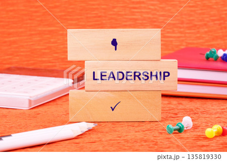 Wooden blocks stacked on an orange surface display LEADERSHIP. A thumbs-down symbol is above the word, with a checkmark below it, illustrating the evaluation of leadership qualities Wooden blocks stacked on an orange surface display LEADERSHIP. A thumbs-down symbol is above the word, with a checkmark below it, illustrating the evaluation of leadership qualities 135819330