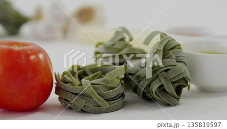 Showing three spinach pasta nests resting on kitchen countertop, with red tomato, garlic and bowls 135819597