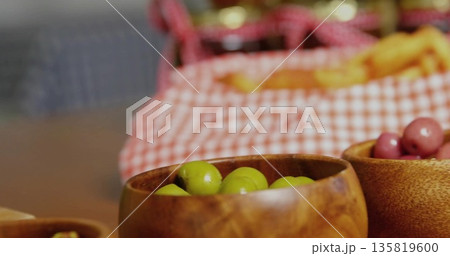 Displaying wooden bowls with green and purple olives on tabletop, gingham cloth, wicker basket Displaying wooden bowls with green and purple olives on tabletop, gingham cloth, wicker basket 135819600