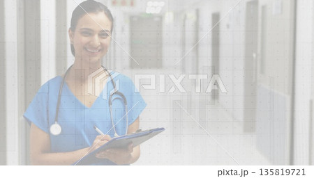 Writing Indian nurse wearing blue scrubs with stethoscope in hospital hall with clipboard and pen 135819721