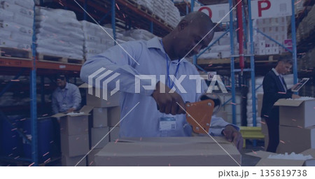 Sealing warehouse worker using tape dispenser at packing station, with supervisor checking tablet 135819738