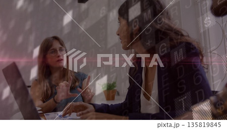 Gesturing glasses woman discussing notes with colleague in office, with laptop papers code patterns 135819845