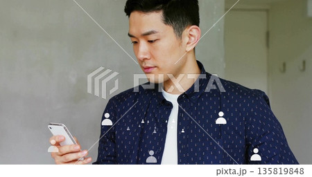 Holding smartphone, adult Asian man scrolling screen in simple home office, copy space 135819848