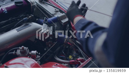 Mechanic wearing coveralls and glove inspecting aluminum intake pipe in garage, with silicone hoses 135819939