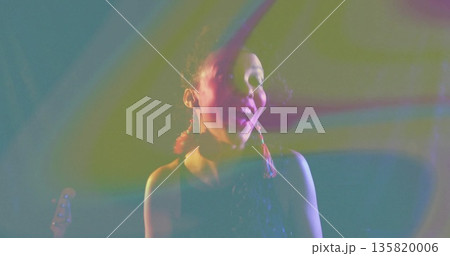 Singing performer wearing sequin top onstage, with colored lights, smoke haze and guitar headstock Singing performer wearing sequin top onstage, with colored lights, smoke haze and guitar headstock 135820006