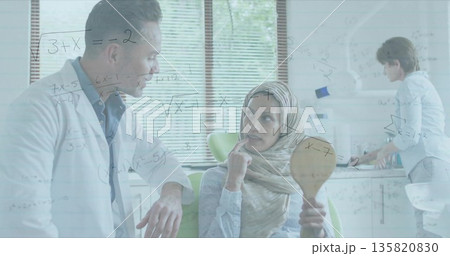 Leaning male doctor speaking with seated patient in bright clinic room, with handheld mirror 135820830