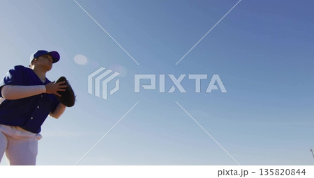 Teenage girl wearing blue jersey, cap raising black glove on field under clear sky, copy space 135820844