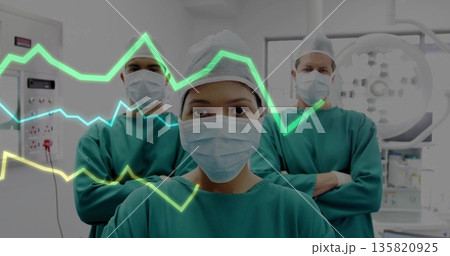 Standing woman in green scrubs checking data in operating room, with console and waveform overlay 135820925