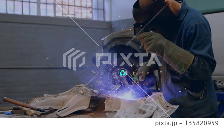 Welding technician directing torch at car body in workshop, wearing helmet, with sparks, copy space 135820959