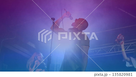 Gripping microphone singer belting out song on stage, with red maracas and colored LED lights 135820981