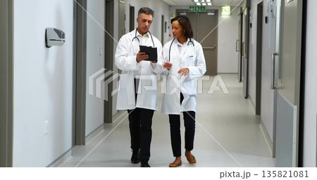 Walking doctor duo reviewing clipboard notes in hospital corridor, with stethoscopes and lab coats 135821081