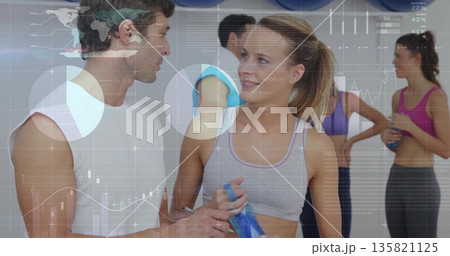 Two participants in sportswear talking in fitness studio with blue water bottles, exercise balls 135821125