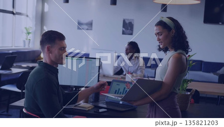 Standing Hispanic woman presenting data on laptop to colleague in office with monitors, copy space 135821203