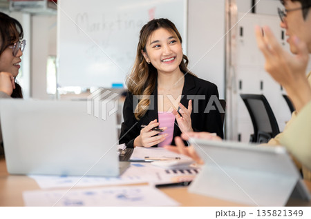 Asian businesswoman explaining in front of laptop as discussing or planning with coworkers in office Asian businesswoman explaining in front of laptop as discussing or planning with coworkers in office 135821349