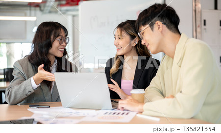 Smiling asian businesswoman and coworkers talking in front of a laptop while making a plan in office 135821354