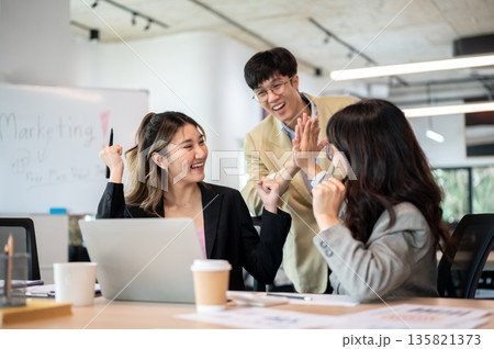 Asian businesswoman and coworker looking excited while raising a fist and clapping hands in office. Asian businesswoman and coworker looking excited while raising a fist and clapping hands in office. 135821373