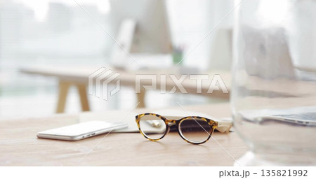 Featuring tortoiseshell glasses resting on wood desk in office, smartphone, laptop, water glass Featuring tortoiseshell glasses resting on wood desk in office, smartphone, laptop, water glass 135821992