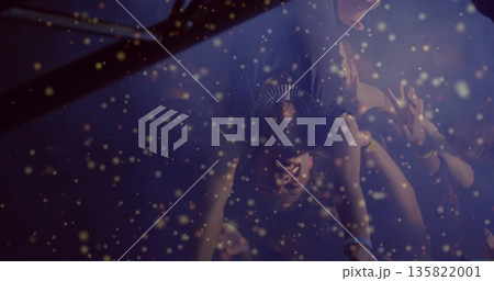 Lifting crowd-surfer upside down at concert under metal truss lights, with golden confetti drifting 135822001