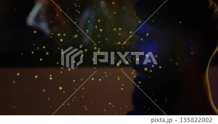 Gazing bearded man observing golden particles drifting in studio, with blurred figures copy space 135822002