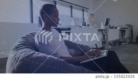 Black woman typing on laptop in fabric beanbag chair in modern office, copy space Black woman typing on laptop in fabric beanbag chair in modern office, copy space 135822028