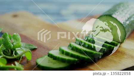 Displaying halved cucumber with sliced rounds on kitchen prep board, floating globe map with greens 135822058