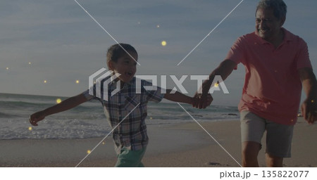 Holding hands and running grandfather and grandson along sandy beach at ocean edge, golden glow 135822077