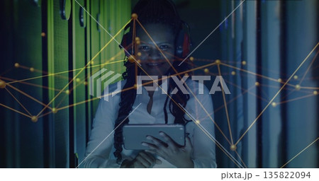 IT engineer analyzing network graph in LED-lit server rack aisle, with tablet, red headphones IT engineer analyzing network graph in LED-lit server rack aisle, with tablet, red headphones 135822094