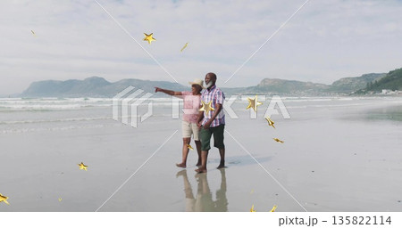 Senior couple strolling barefoot on wet sandy shoreline at low tide, with wide-brimmed sun hat Senior couple strolling barefoot on wet sandy shoreline at low tide, with wide-brimmed sun hat 135822114
