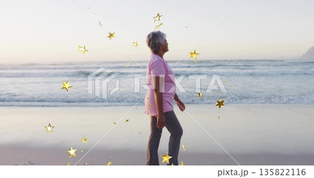 Walking woman in pink polo and gray pants on sand at sunset, with digital star overlays 135822116