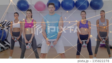 Man in turquoise top lifting kettlebell in gym, with stability balls, bikes and nodes overlay 135822278
