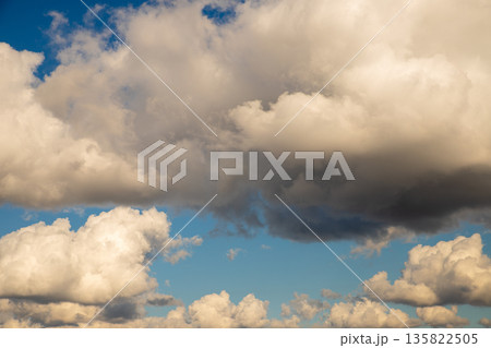 Fluffy cumulus clouds against a clear blue sky, illuminated by warm sunset light. Natural background for weather forecast or beautiful sky scene. Fluffy cumulus clouds against a clear blue sky, illuminated by warm sunset light. Natural background for weather forecast or beautiful sky scene. 135822505