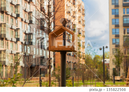 A wooden bird feeder in the courtyard of a modern apartment complex. Family, housing, mortgage, affordable credit 135822508
