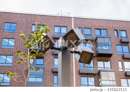 Modern outdoor lighting complex with multiple LED luminaires on single pole for urban illumination. Three consoles on single support, facing in different directions and at different angles Modern outdoor lighting complex with multiple LED luminaires on single pole for urban illumination. Three consoles on single support, facing in different directions and at different angles 135822513