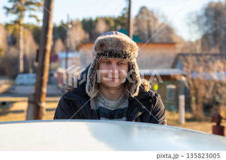 man wearing fur winter hat stands in front of his car and opens it to go to work on a sunny, frosty day. ex-smoker 135823005