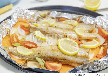 Prerape raw spiced hake for a bake in the oven with lemon, tomatoes, carrots, and onions in foil. Delicious fish for lunch or dinner, perfect for a diet. Tasty and fresh  hake fish for bake with 135823124