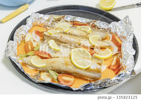 Prerape raw spiced hake for a bake in the oven with lemon, tomatoes, carrots, and onions in foil. Delicious fish for lunch or dinner, perfect for a diet. Tasty and fresh  hake fish for bake with 135823125