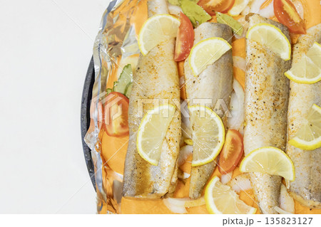 Prerape raw spiced hake for a bake in the oven with lemon, tomatoes, carrots, and onions in foil. Delicious fish for lunch or dinner, perfect for a diet. Tasty and fresh  hake fish for bake with 135823127