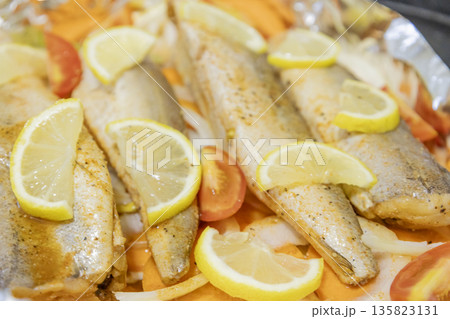 Prerape raw spiced hake for a bake in the oven with lemon, tomatoes, carrots, and onions in foil. Delicious fish for lunch or dinner, perfect for a diet. Tasty and fresh  hake fish for bake with 135823131