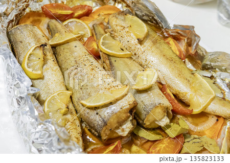 Spiced hake baked in the oven with lemon, tomatoes, carrots, and onions in foil. Delicious fish for lunch or dinner, perfect for a diet. Tasty hake fish baked with vegetables. 135823133
