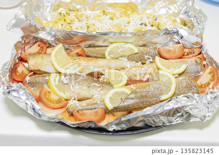 Prerape raw spiced hake for a bake in the oven with lemon, tomatoes, carrots, and onions in foil. Delicious fish for lunch or dinner, perfect for a diet. Tasty and fresh  hake fish for bake with 135823145