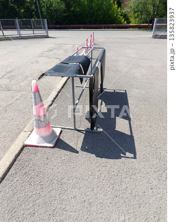 Car floor mats are hung over a makeshift metal rack near traffic cones on asphalt, suggesting they are being dried or aired out on a bright, sunny day 135823937